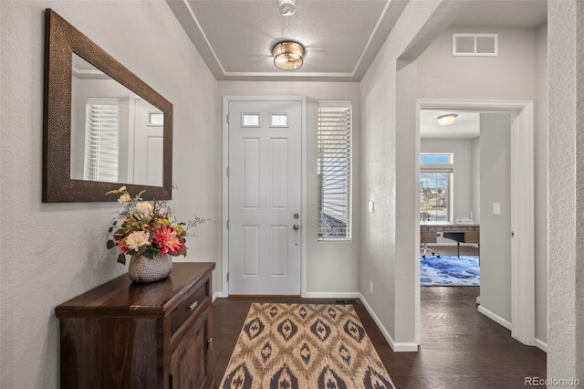 entrance foyer featuring dark wood-style floors, baseboards, visible vents, and a textured wall