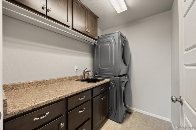 clothes washing area featuring cabinet space, baseboards, stacked washer / dryer, a textured ceiling, and a sink