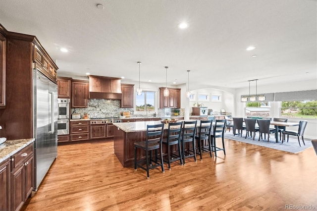 6331 County Road 32, Platteville, CO 80651 - kitchen featuring appliances with stainless steel finishes, premium range hood, light wood finished floors, a breakfast bar area, and decorative backsplash