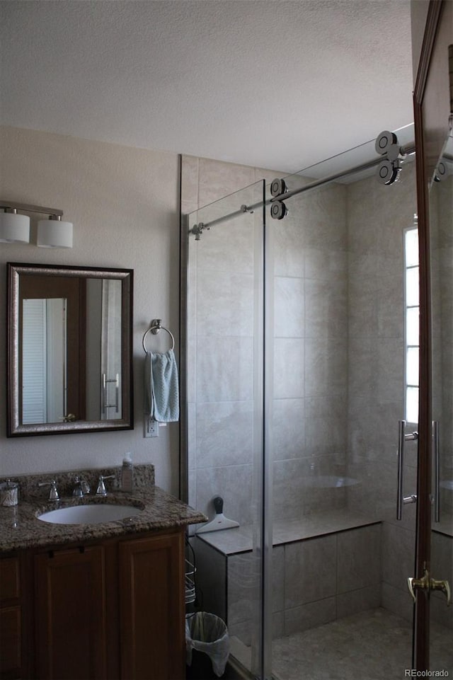 full bath with a shower stall, a textured ceiling, and vanity