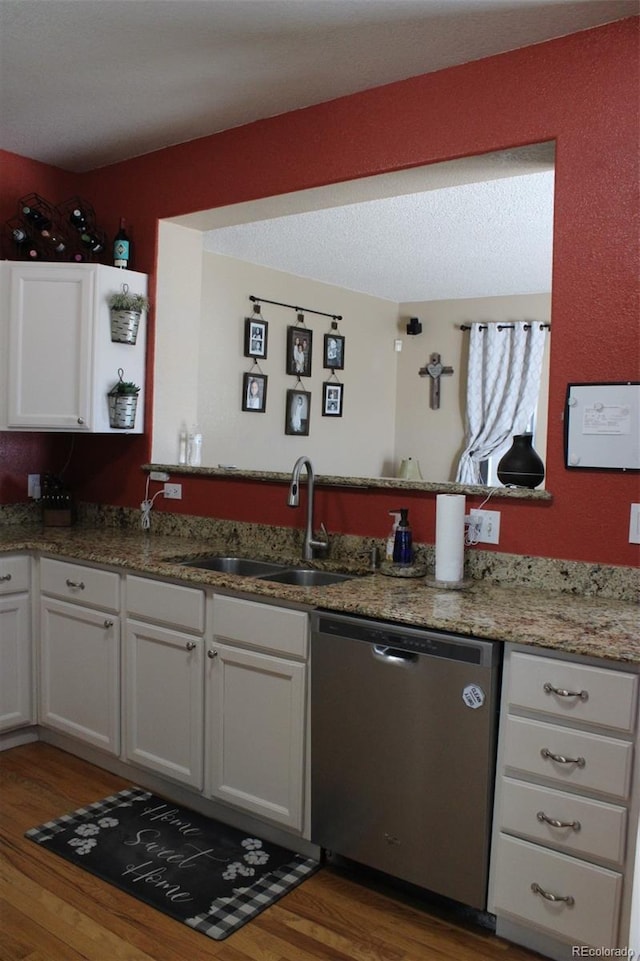 kitchen with light stone counters, wood finished floors, white cabinetry, a sink, and stainless steel dishwasher