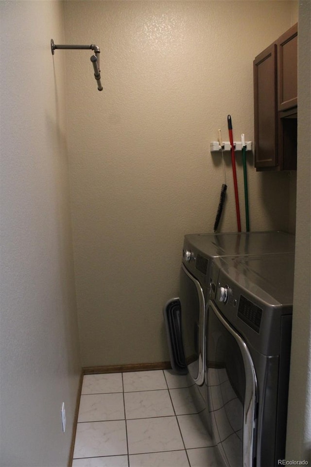 clothes washing area featuring washer and dryer, light tile patterned floors, cabinet space, and baseboards