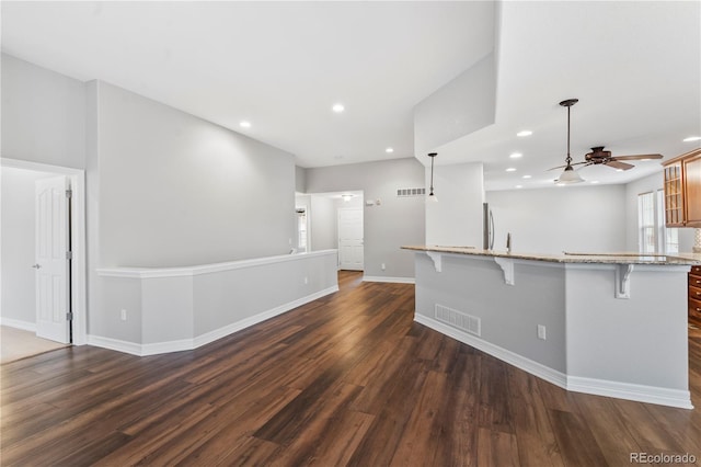 kitchen with visible vents, a breakfast bar area, light stone counters, recessed lighting, and dark wood-style floors