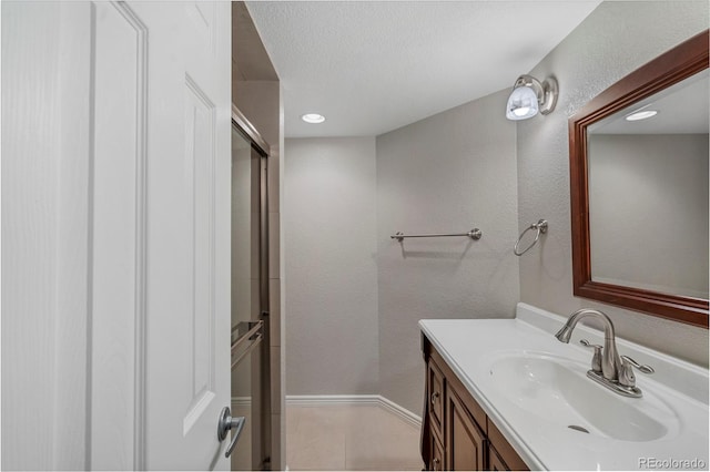 bathroom with vanity, baseboards, tile patterned flooring, a textured ceiling, and a textured wall