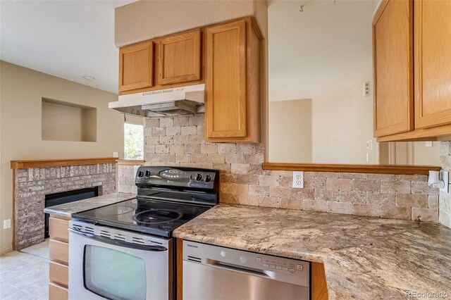 2035 Overland Dr, Brighton, CO 80601 - kitchen with under cabinet range hood, appliances with stainless steel finishes, tasteful backsplash, and a brick fireplace