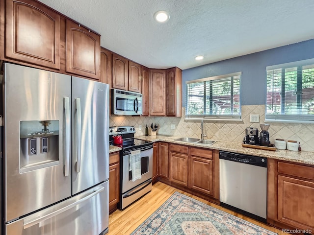 6664 Gray St, Arvada, CO 80003 - kitchen with appliances with stainless steel finishes, light wood finished floors, a textured ceiling, decorative backsplash, and brown cabinets