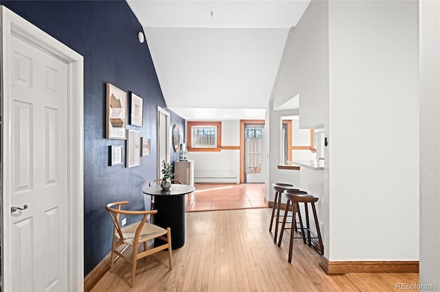 corridor with baseboard heating, baseboards, vaulted ceiling, and light wood finished floors