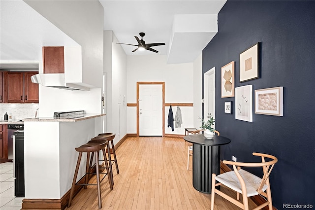 kitchen with a breakfast bar area, light countertops, decorative backsplash, a ceiling fan, and light wood-type flooring