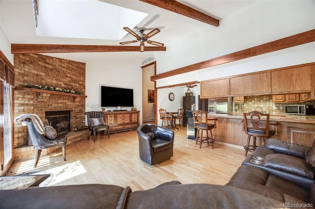 living area featuring a fireplace, beamed ceiling, a ceiling fan, light wood finished floors, and a skylight