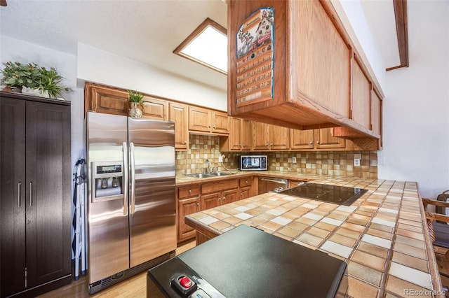 kitchen featuring appliances with stainless steel finishes, a sink, tile countertops, a peninsula, and tasteful backsplash