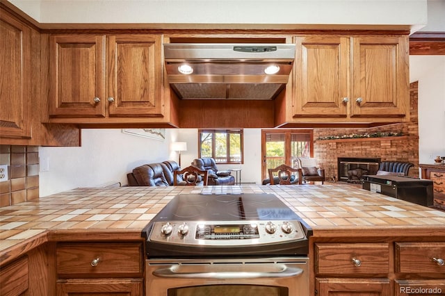 kitchen with tile counters, stainless steel range with electric stovetop, brown cabinets, and extractor fan