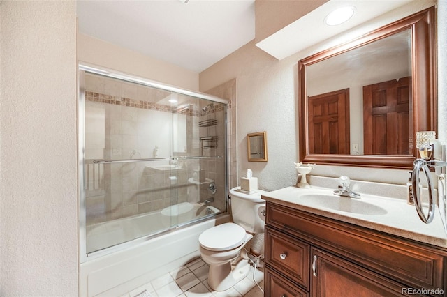 full bath with vanity, bath / shower combo with glass door, tile patterned floors, toilet, and a textured wall