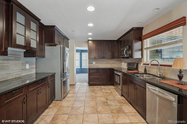 kitchen with appliances with stainless steel finishes, tasteful backsplash, dark brown cabinetry, sink, and dark stone countertops