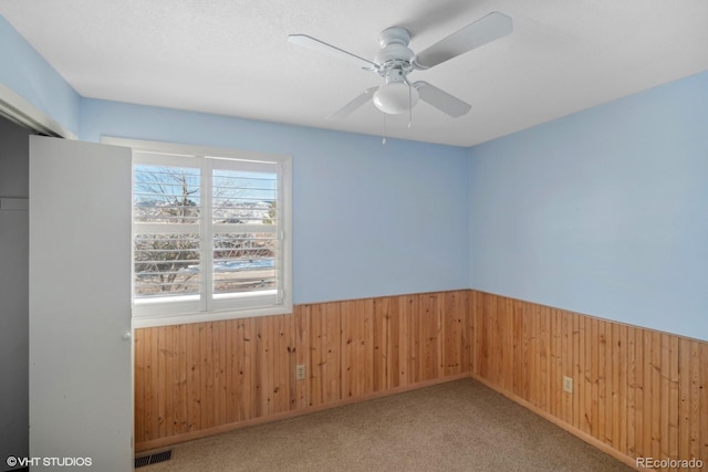 carpeted empty room featuring ceiling fan and wooden walls