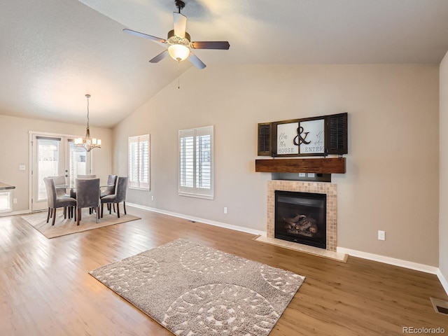 dining space with a healthy amount of sunlight, a tiled fireplace, vaulted ceiling, and wood finished floors