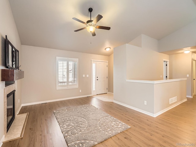 unfurnished living room with visible vents, a ceiling fan, a glass covered fireplace, vaulted ceiling, and wood finished floors