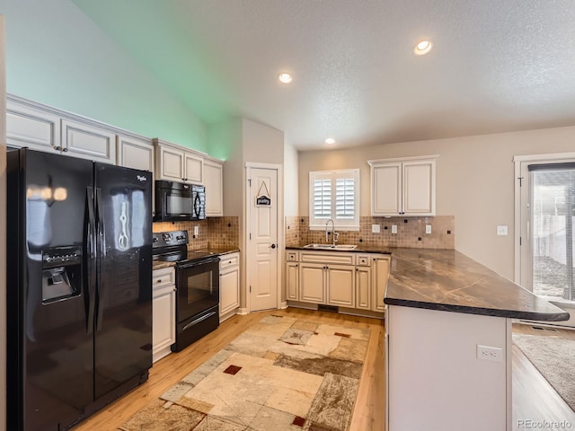 kitchen with a peninsula, a sink, backsplash, black appliances, and dark countertops