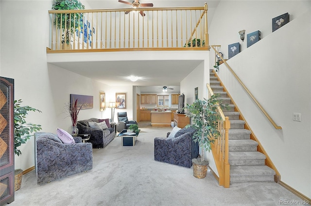 carpeted living area with a high ceiling, stairway, a ceiling fan, and baseboards