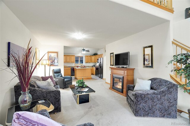 living area with light carpet, ceiling fan, and a glass covered fireplace