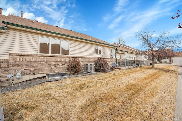 view of property exterior featuring central AC unit, a lawn, fence, and brick siding