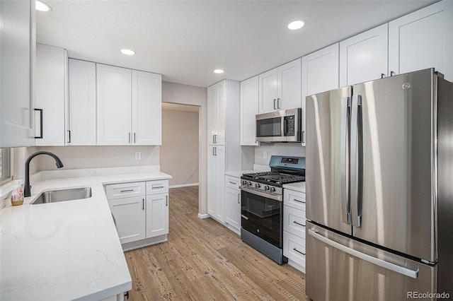 kitchen with light stone countertops, light wood-type flooring, white cabinets, stainless steel appliances, and a sink