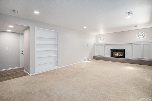 unfurnished living room with a glass covered fireplace, built in features, visible vents, and carpet floors