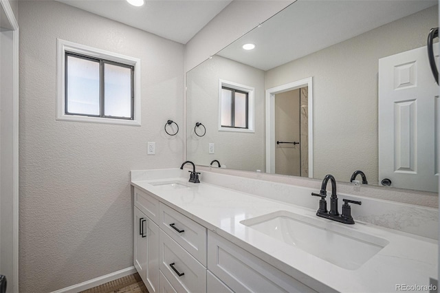 bathroom with a sink, baseboards, double vanity, and a textured wall