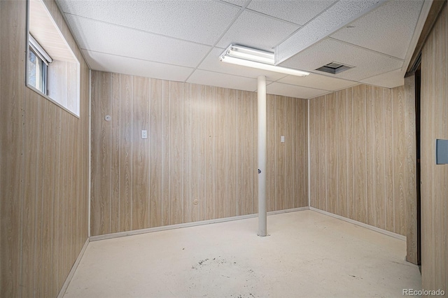 basement featuring wooden walls, visible vents, baseboards, and a drop ceiling