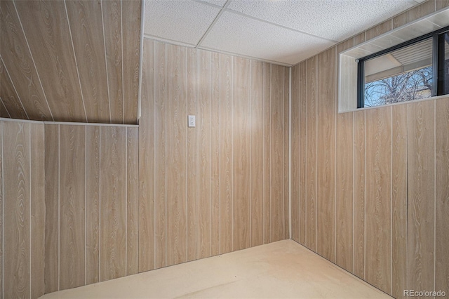 empty room featuring a drop ceiling and wood walls