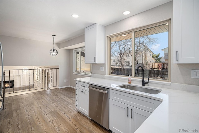 kitchen featuring light wood-type flooring, a sink, white cabinets, dishwasher, and hanging light fixtures