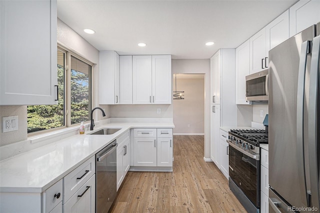 kitchen with a sink, light wood-type flooring, appliances with stainless steel finishes, and white cabinets