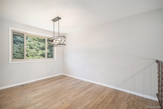 spare room with a chandelier, visible vents, light wood-style flooring, and baseboards