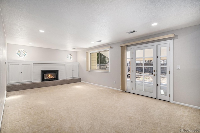 unfurnished living room with a glass covered fireplace, carpet flooring, baseboards, and a textured ceiling