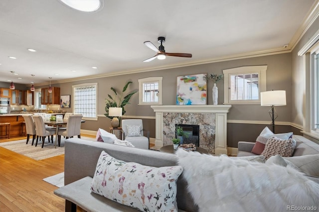 living area with a fireplace, crown molding, recessed lighting, light wood-style floors, and baseboards