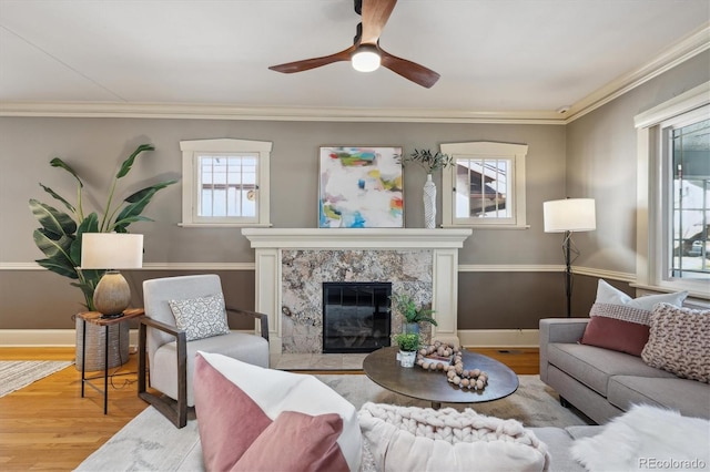 living area featuring baseboards, ceiling fan, ornamental molding, wood finished floors, and a fireplace