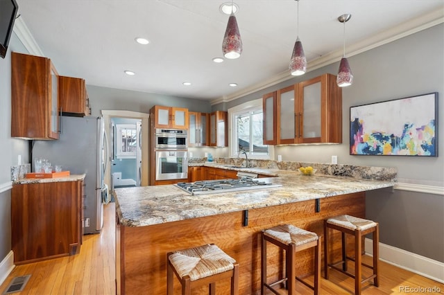 kitchen featuring stainless steel appliances, visible vents, brown cabinetry, a sink, and a peninsula