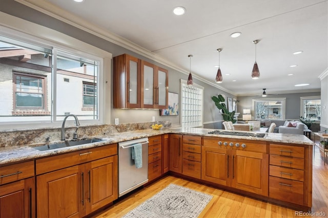 kitchen with brown cabinetry, appliances with stainless steel finishes, a peninsula, light stone countertops, and a sink