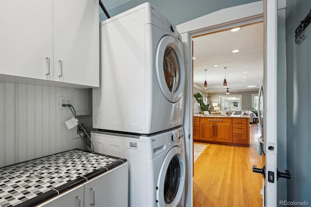 laundry area with cabinet space, light wood-style flooring, stacked washer / dryer, and recessed lighting