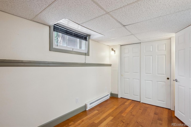 unfurnished bedroom with a drop ceiling, a baseboard radiator, wood finished floors, baseboards, and a closet