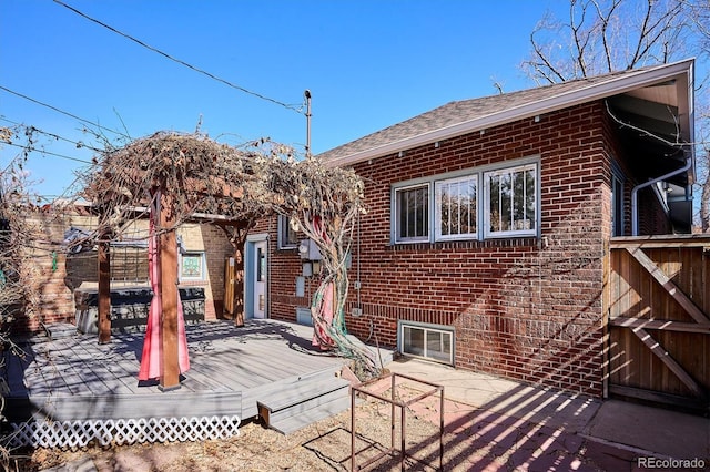 back of property featuring brick siding, a deck, and roof with shingles