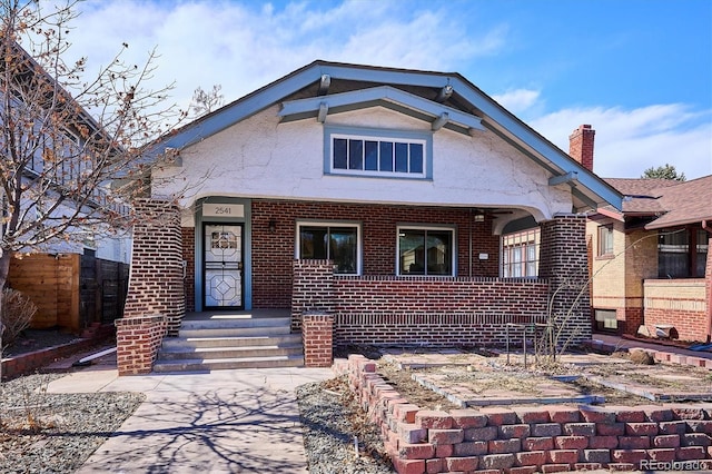 view of front of home featuring a porch, brick siding, fence, and stucco siding