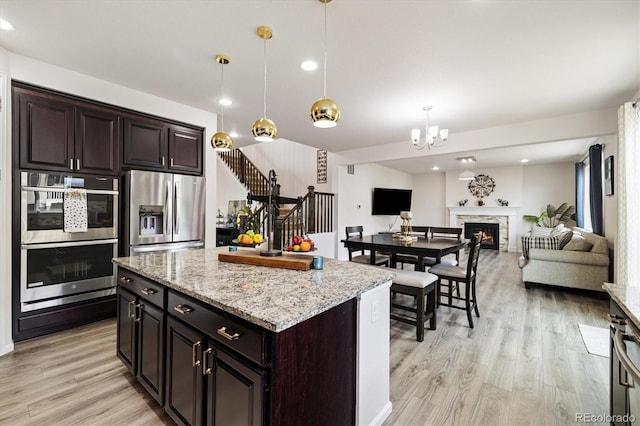 kitchen with a kitchen island, decorative light fixtures, appliances with stainless steel finishes, open floor plan, and light wood-style flooring