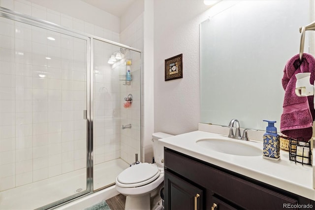 bathroom featuring toilet, a textured wall, a shower stall, and vanity