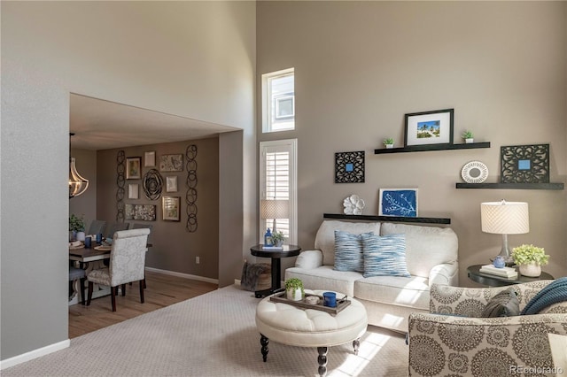 living room featuring a chandelier, baseboards, a high ceiling, and wood finished floors
