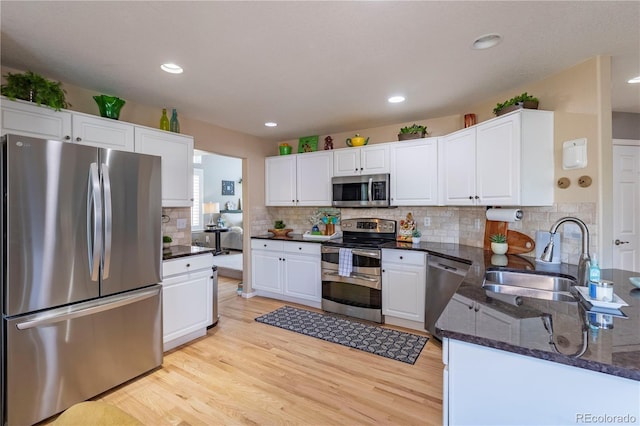 kitchen with a sink, light wood-style floors, white cabinetry, dark stone counters, and stainless steel appliances