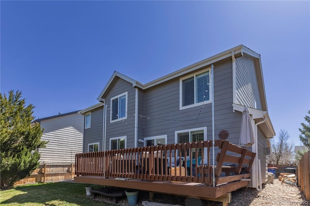 back of property with a deck, fence, and a lawn