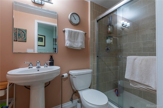 bathroom with toilet, a stall shower, a sink, and baseboards