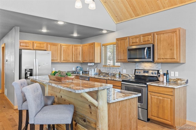 kitchen with sink, a kitchen island, stainless steel appliances, light stone countertops, and a kitchen bar