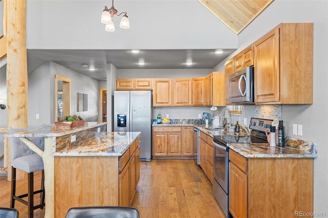 kitchen with vaulted ceiling, pendant lighting, sink, a kitchen breakfast bar, and stainless steel appliances