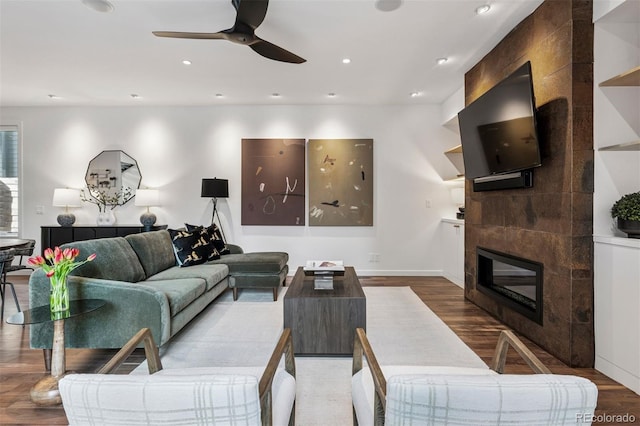 living area with a ceiling fan, a fireplace, wood finished floors, baseboards, and recessed lighting